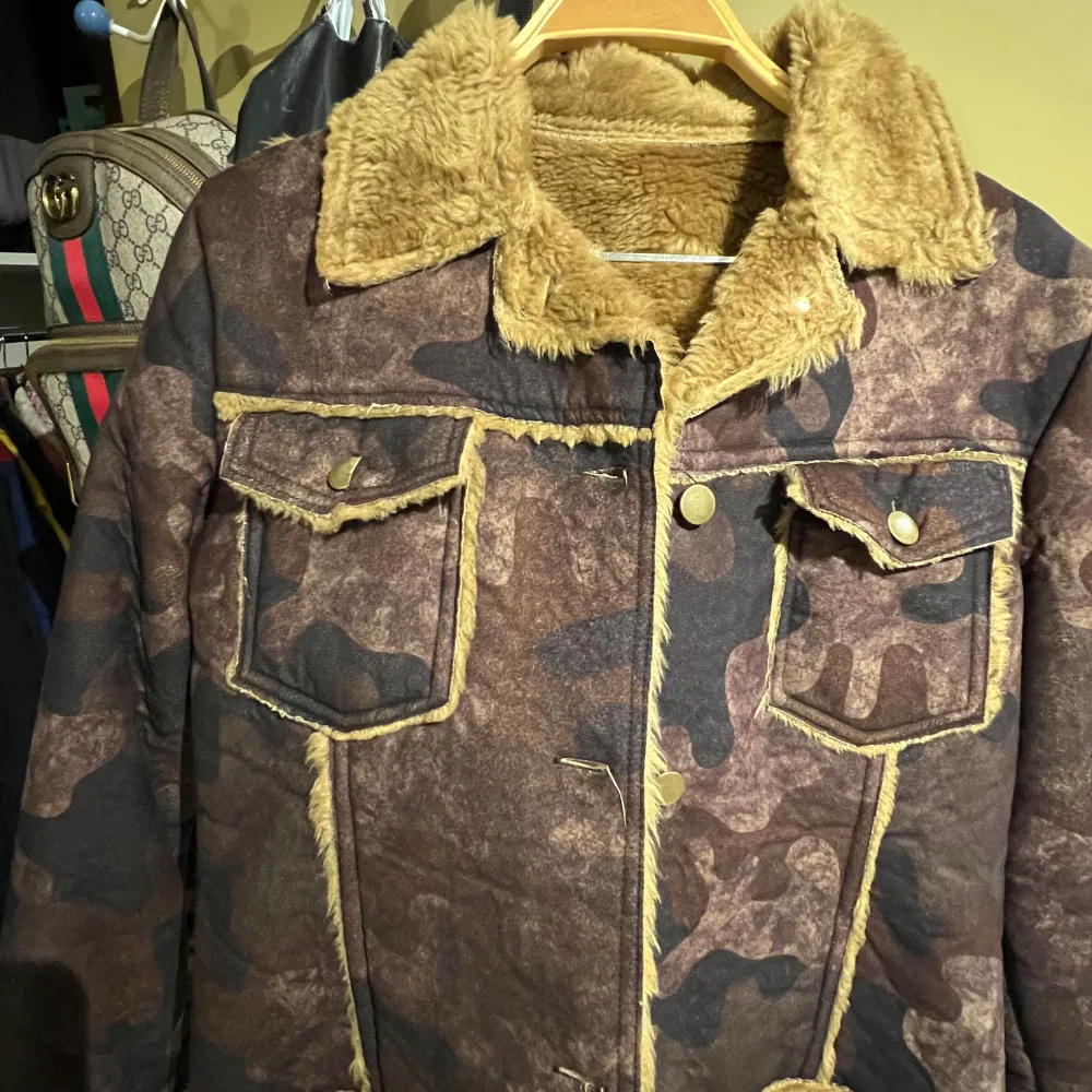 Säljer en cool camouflagejacka med fuskpälsdetaljer. Jackan har en mjuk krage och nederkant i beige fuskpäls, samt knappar framtill. Perfekt för höst och vinter, och den är i mycket bra skick. Tillverkad i Italien av 95% polyester.. Jackor.