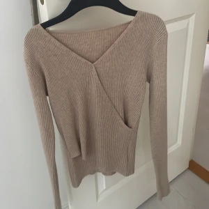 Beige ribbad omlottopp - Säljer en superfin beige ribbad omlottopp med lång ärm. Perfekt för höst och vår, den är både stilren och bekväm. Passar till både vardag och fest! 💫