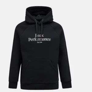 Svart hoodie från Peak Performance - Säljer en svart hoodie från Peak Performance med vit text på bröstet. Den har en klassisk känguruficka och justerbar huva med dragsko. Perfekt för både vardag och chill. 🖤