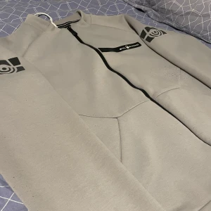 Grå tech jacka/kofta från Sail Racing - Säljer en grå tech jacka/kofta från Sail Racing i nyskick. Perfekt för hösten/vintern, tillverkad i polyester och bomull så väldigt bekväm, håller även värmen riktigt bra. Passar både till vardags och lite mer sportiga aktiviteter.