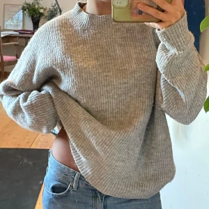 Grå stickad tröja - Mjuk grå stickad tröja i oversized passform. Perfekt för kyliga dagar med sin ribbade struktur och långa ärmar. Enkel att matcha med jeans! 