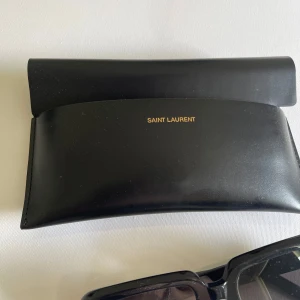Svarta solglasögon från Saint Laurent - Saint Laurent Solglasögon SL 534 SUNRISE-001 52 - Klassisk Svart Design med Originalfodral Säljer ett par tidlösa Saint Laurent-solglasögon i klassisk svart design.Somlglasögon utstrålar elegans och kvalitet och är perfekta för dig som vill ha en stilren och lyxig accessoar. Notera att det finns tydliga tecken pa användning med repor på bågen, men glasen är i gott skick utan repor (skicar fler bilder).  • Inköp  för 315 euro fran Mytheresa den 9 februari 2023. • Orderbekräftelse finns via e-post