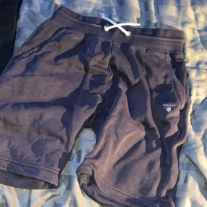 Mörkblå shorts från GANT - Säljer ett par snygga mörkblå shorts från GANT i mycket bra skick. De har en bekväm passform med snörning i midjan och är perfekta för sommarens alla äventyr. Materialet känns mjukt och skönt, perfekt för både vardag och träning.