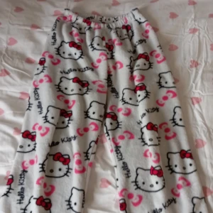 Hello Kitty mjukisbyxor - Supermysiga Hello Kitty mjukisbyxor i vit färg med ett gulligt mönster av Hello Kitty-ansikten och rosa rosetter. Perfekta för en chill dag hemma eller som pyjamasbyxor. De har en elastisk midja för extra komfort.