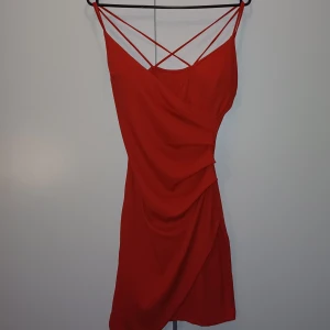 Röd lite tjatare klänning - En röd lite tajtare klänning. Den har fastsydd vadering. Banden korsas i bak. Perfekt för en middag elller liknande. Passar både S och M. Den är köpt på en marknad därav inget märke på den.