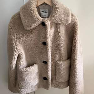 Säljer en supermysig beige teddyjacka från Zara. Den har stora knappar och två praktiska fickor framtill. Perfekt för höst och vinter när du vill hålla dig varm och stilren. Jackan har en normal passform. Perfekt för att mysa till vardagsoutfiten!