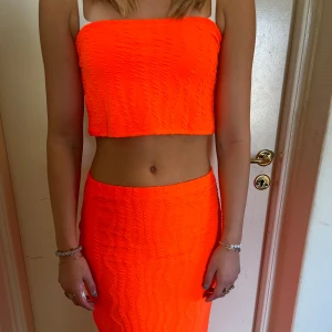 Neonorange croppad topp - Säljer ett super snyggt neonorange sett innerhållande en croppad topp med en texturerad yta, den är även armlös likadant men kjolen texturersd yta lång kjol. Den har en tight passform som framhäver figuren. 
