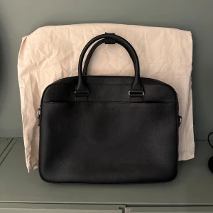 Tiger of Sweden datorväska - En svart datorväska i läder från Tiger. Köpt på Åhléns till ett nypris på ungefär 2500kr. Perfekt nu till skolstart eller jobbet. Skicket är 9/10 då den inte har några tydliga defekter. Skriv vid frågor!