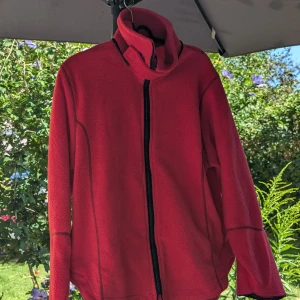 Röd fleecejacka - Supermysig röd fleecejacka i 100% polyester, perfekt för kyliga dagar. Den har en dragkedja framtill och en hög krage som håller dig varm. Tillverkad i Nepal, vilket ger den en unik touch. Perfekt för höst- och vinteräventyr!Dragkedjan är trasig 