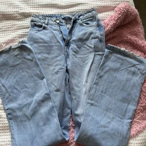 Ljusa jeans med slitningar - Säljer ett par ljusa högmidjade  jeans med coola slitningar på benen. De har en klassisk femficksdesign och stängs med dragkedja och knapp. Perfekta för en avslappnad och trendig look!