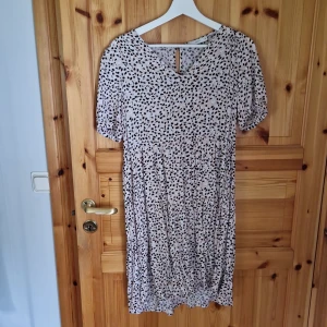 Ljusrosa prickig klänning - Säljer en superfin ljusrosa klänning med svarta och vita prickar. Den har korta ärmar och en bekväm passform som är perfekt för både vardag och fest. Materialet känns mjukt och luftigt, vilket gör den idealisk för varmare dagar.