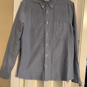 Blå Oxford-skjorta från Asket - Snygg blå Oxford-skjorta från Asket i storlek S. Skjortan har en klassisk design med knappar och en bröstficka. Perfekt för en stilren look.
