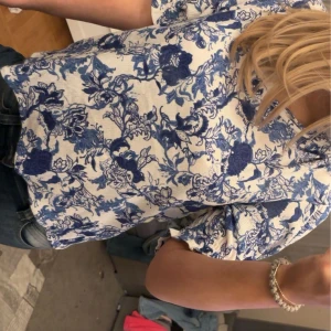 Blåvit blommig blus - Säljer en söt blus med blått blommönster. Blusen har korta ärmar och en avslappnad passform, perfekt för en somrig dag. Från Lindex helt oanvänd med prislapp kvar. Storlek M