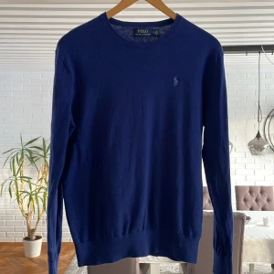 Mörkblå tröja från Polo Ralph Lauren - Säljer en stilren mörkblå tröja från Polo Ralph Lauren med en liten broderad logotyp på bröstet. Tröjan har långa ärmar och en rund halsringning. Perfekt för en klassisk och avslappnad look.