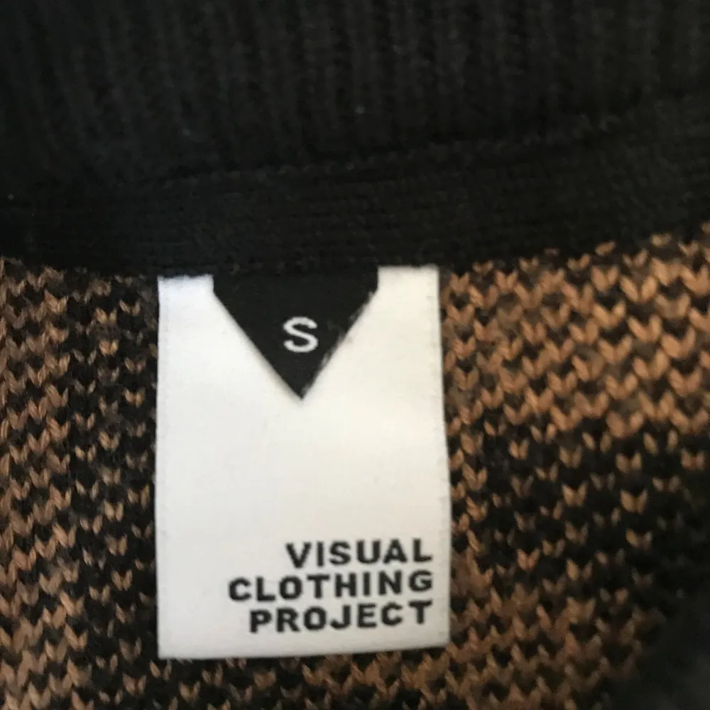 Säljer en unik svart och beige tröja från Visual Clothing Project med ett geometriskt mönster. Tröjan har långa ärmar och en rund halsringning. Perfekt för att sticka ut i mängden!. Neuletakit & Villapaidat.