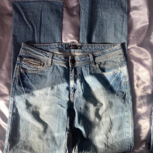 Blå jeans från Lindex - Säljer ett par klassiska blå jeans från Lindex. De har en straight passform och är dekorerade med nitar på fickorna. Perfekta för en avslappnad stil. OBS! Lagade i skrevet. 