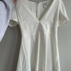 Vit klänning från Monki - Säljer en stilren vit klänning från Monki med v-ringning och korta ärmar. Perfekt för en somrig look. Klänningen har en enkel och elegant design som passar till många tillfällen.