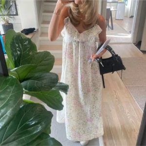 Blommig sommarklänning med volangdetaljer - Charmig långklänning med blommigt mönster i ljusa färger. Klänningen har smala axelband och volangdetaljer vid bysten, vilket ger en romantisk touch. Perfekt för varma sommardagar.