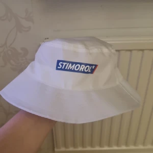 Vit hatt med Stimorol-logga - Säljer en vit hatt med Stimorol-logga framtill. Hatten är tillverkad i 100% polyester och har en klassisk design med bred brätte. Perfekt för soliga dagar!