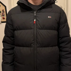 Svart pufferjacka från Tommy Hilfiger - Säljer en svart pufferjacka från Tommy Hilfiger med broderad logga på bröstet. Jackan har en dragkedja framtill och är långärmad. Perfekt för kyliga dagar med sin varma och vadderade design.