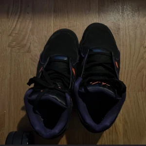 Nike Air sneakers i svart och lila - Snygga Nike Air sneakers i svart med lila och orange detaljer. Skorna har en klassisk snörning och en bekväm passform. Perfekta för dig som vill ha en stilren look med en färgklick.