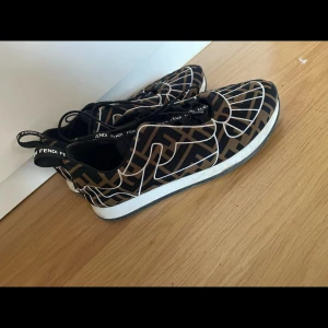 Mönstrade sneakers från Fendi - Snygga sneakers från Fendi med ett unikt mönster i svart och beige. Skorna har en vit sula och en praktisk dragflik baktill för enkel påtagning. Perfekta för en stilren look.