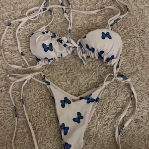Vit bikini med blå fjärilar - Snygg vit bikini med blå fjärilar och knytband. Toppen har justerbara band och bygel för extra stöd. Trosan har knyt i sidorna för perfekt passform. Perfekt för sommarens stranddagar! Fraktar endast varan och köparen betalar frakten! Priset som syns är det som gäller🫶🙏