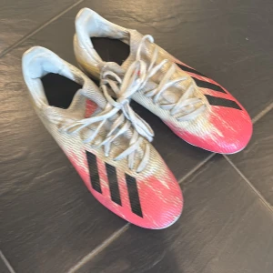 Adidas fotbollsskor i röd och vit - Snygga Adidas fotbollsskor i röd och vit med svarta detaljer. Skorna har snörning och dobbar för bra grepp på planen. Perfekta för fotbollsspelare som vill ha stil och funktionalitet.