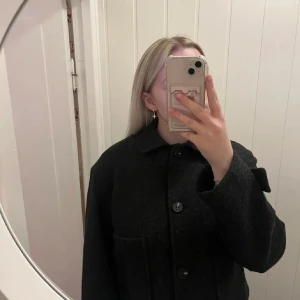 Kort kappa - Säljer en stilren gråsvart kappa från 157 i storlek S. Den har en klassisk design med stora knappar och två fickor framtill. Perfekt för höst, vinter och vår, och ger en elegant touch till vilken outfit som helst. Passar både till vardags och festliga tillfällen. Använd ett fåtals gånger, som ny! nypris 400kr
