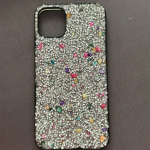 Glittrigt mobilskal med färgglada stenar ( iPhone 11 PRO Max) - Snyggt mobilskal med en glittrig yta och färgglada stenar. Perfekt för att ge din mobil en unik och iögonfallande look. Skalet är designat för att passa en fyrkantig kameramodul och har en robust konstruktion.