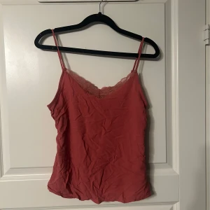 Korall linnetopp med spetsdetaljer - Säljer en söt korall linnetopp med smala axelband och spetsdetaljer vid halsringningen. Perfekt för varma dagar eller som ett lager under en tröja. Toppen har en mjuk och bekväm passform.