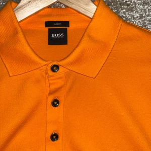 Orange pikétröja från Boss - Snygg orange pikétröja från Boss. Aldrig använd. Perfekt till sommaren! 