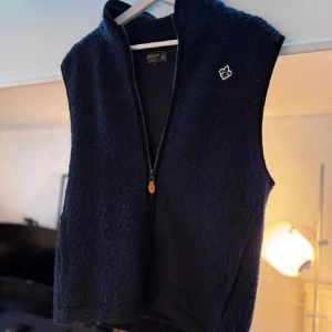 Marinblå Morris fleeceväst - Säljer en Marinblå fleeceväst med dragkedja och ett broderat Morris märke på bröstet. Perfekt för att hålla värmen under kyliga dagar. Västen har en enkel och stilren design. Nypris 2400kr                                                   Kontakta mig vid frågor!