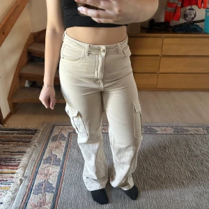 Beige cargobyxor - Snygga beige cargobyxor med hög midja och praktiska fickor på sidorna. Byxorna har en loose passform och är perfekta för en avslappnad stil. Tillverkade i ett bekvämt material som ger en skön känsla hela dagen.