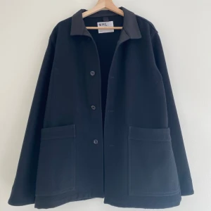 Margaret Howell Svart Overshirt / Jacka - Stilren svart overshirt från Margaret Howell med knappar framtill och stora fickor. Jackan har en krage i lite annat material, resten av jackan är i filtmaterial. Storlek L men sitter oversized, mer likt en XL. 