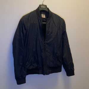 Svart bomberjacka från Lee - Storlek M men sitter som S. Snygg svart bomberjacka från Lee med dragkedja framtill. Jackan har en klassisk design med ribbade muddar vid ärmslut och nederkant. Perfekt för en stilren look.