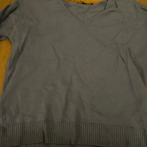 Grå/blå v-ringad tröja från 157 - Säljer en stilren grå tröja från 157 med v-ringning. Tröjan har långa ärmar och ribbade kanter vid ärmslut och nederkant. Perfekt för en avslappnad look. Har inte använt på länge därför kan den vara lite skrynklig. Men annars bra skick k strl M
