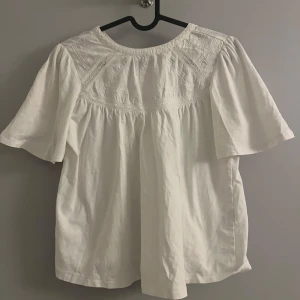 Vit blus med spetsdetaljer - Säljer en söt vit blus med spetsdetaljer på överdelen. Blusen har korta ärmar och en lös passform, perfekt för en avslappnad stil. Den är tillverkad i ett lätt och bekvämt material.