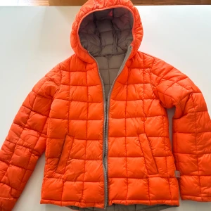 Orange quiltad dunjacka med huva - Klassisk lite sportig dunjacka i klar orange färg med quiltat mönster och huva. Märke Benetton. Tjockare i mtrl dvs ine klassisk lättdun. Väldigt skön och passar till både vardag, träning mm