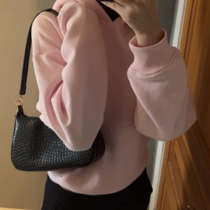 Svart axelväska i skinn - Snygg svart axelväska i skinn med en stilren design. Väskan har en enkel axelrem och en praktisk storlek för vardagliga behov. Perfekt för att bära med sig det viktigaste.