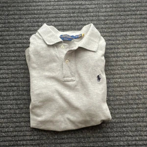 Grå pikétröja från Ralph Lauren - Säljer en stilren grå pikétröja från Ralph Lauren med klassisk krage och två knappar. Storleken är lite mindre på den 