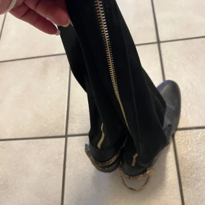 Svarta boots med dragkedja och kedjedetalj från Paolo  Bocelli  - Snygga svarta boots i skinn med dragkedja längs sidan och en cool kedjedetalj runt ankeln. Perfekta för en stilren look.Paolo Bocelli Stövlar, Svart, EUR 37