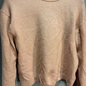 Ljus rosa stickad tröja från H&M - Mysig ljus rosa stickad tröja från H&M. Perfekt för kyliga dagar med sin mjuka och bekväma passform. Tröjan har långa ärmar och en klassisk rund halsringning.