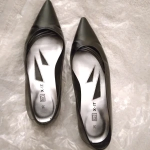 Svarta pumps / ballerinaskor från X-IT, fint skick. Storlek 36. - Eleganta svarta pumps/ballerinaskor med liten klack, från X-IT.  Perfekta för både vardag och fest. Stilren design med spetsig tå och snygg silverfärgad insida och dekorerande detalj i form av små remmar. Endast använda kort stund vid 1 tillfälle, så i princip nyskick, hela och rena. Skickas tillsammans med tillhörande skokartong.