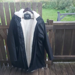 Svart jacka med foder från Strova - Säljer en svart jacka från Strova i storlek XL. Den har ett mysigt vitt foder som ser supervarmt ut, perfekt för kalla dagar. Jackan har en huva och långa ärmar, vilket gör den idealisk för höst och vinter. Den är i bra skick och redo för nya äventyr!