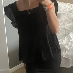 Svart blus med volangdetaljer - Säljer en svart blus med volangdetaljer på ärmarna. Perfekt för både vardag och fest. Aldrig andvänd