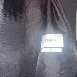 Svart kavaj från Filippa K - Säljer en stilren svart kavaj från Filippa K i storlek 48. Kavajen har en klassisk design med knappar framtill och är perfekt för både formella och semi-formella tillfällen. Materialet känns högkvalitativt och ger en elegant look. Passar perfekt för höst och vinter!