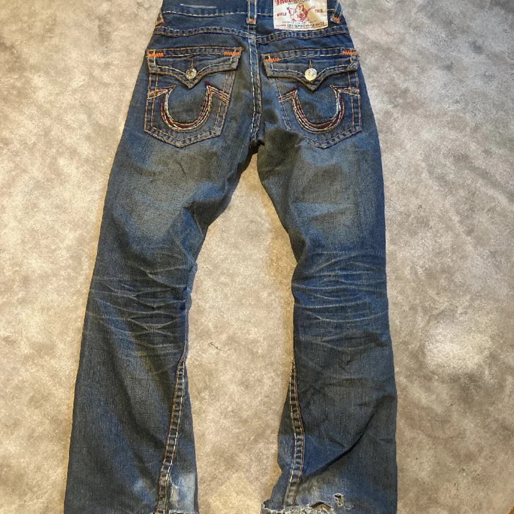 Säljer ett par snygga blå jeans från True Religion. De har en cool design med detaljerade bakfickor och orange sömmar som verkligen poppar. Perfekta för en casual look eller en utekväll. De är i bra skick och redo för en ny ägare!. Jeans & Byxor.