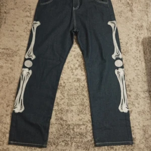 Mörkblå jeans med skelettmönster - Unika mörkblå jeans med coolt skelettmönster längs benen. Perfekta för att sticka ut med en edgy stil. De har en rak passform och bakfickor för extra stil och funktionalitet.