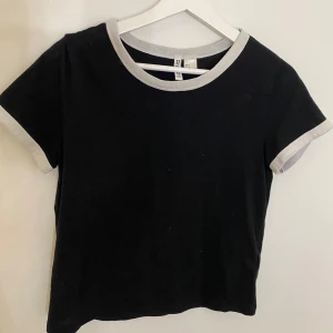 Svart och vit t-shirt - Snygg svart t-shirt med vita kanter vid hals och ärmslut. Ser ut som en magtröja kanske men är längre än så, passar för storlekar beroende på vilken passform man vill ha. skriv vid frågor eller för fler bilder 🤍 öppen för prisförslag